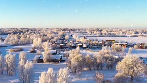Magical-winter-township-and-natural-surroundings-during-snowfall,-aerial-view