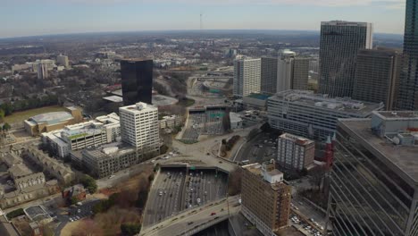 Aerial-drone-shot-slowly-flying-over-the-highway-in-downtown-Atlanta,-Georgia-as-rush-hour-traffic-moves-between-the-skyscrapers-on-a-winter-day