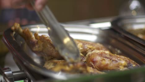 Fired-chicken-thighs-arranged-into-stainless-steel-pan-using-tongs,-filmed-as-close-up