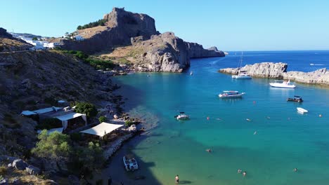Playa-De-Agios-Pavlos-En-Rodas,-Grecia-Con-La-Acrópolis-De-Lindos,-Casas-Y-El-Mar-Mediterráneo-Durante-El-Día-Filmado-Con-El-Drone