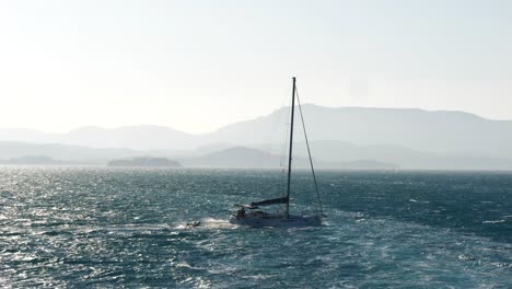 Sailing-boat-navigating-through-the-turbulent-waters-of-the-Ionian-Sea-near-Corfu-Island,-towing-a-pontoon