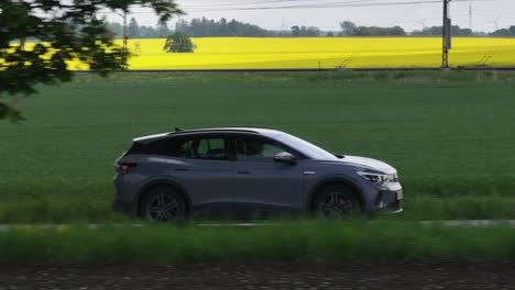 EV-SUV-car-driving-on-road,-yellow-field,-medium-sideview-tracking