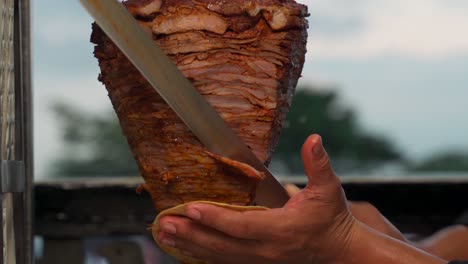 Taquero-cutting-carne-al-pastor-meat-pork-raw-fresh-authentic-from-trompo-kebab-shawarma-grilled-asada-tortilla-in-hand-hot-recipe-latin-mexico