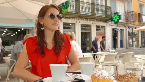 Portugiesische-Frau-Sitzt-Im-Café-Im-Freien-In-Porto,-Portugal,-Mit-Tassen-Kaffee-Und-Gebäck-Auf-Dem-Tisch