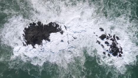 Powerful-ocean-waves-pounding-on-rocky-island,-aerial-top-down-view
