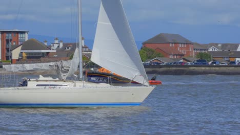 Yacht-passing-lifeboat-on-river-as-lifeboat-crew-start-to-disembark