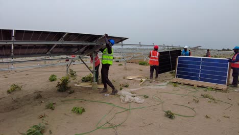 Group-Of-Men-With-Engineers-And-Technicians-Installing-Photovoltaic-Panel-At-Solar-Farm-Project-In-Jambur,-Gambia-West-Africa