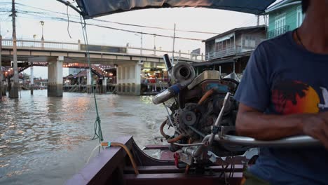 A-boatman-is-steering-his-motorized-wooden-boat-in-the-canal-of-Amphawa-Floating-Market,-Thailand
