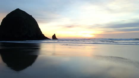 Die-Farben-Des-Sonnenuntergangs-Spiegeln-Sich-Im-Sand-Am-Canon-Beach,-Oregon