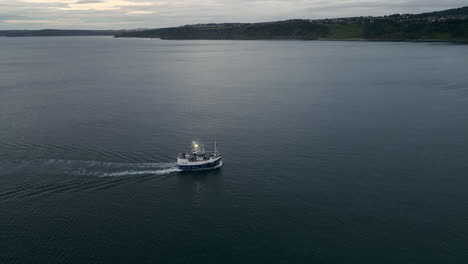 Drone-Shot-of-Fishing-Boat-Heading-Inland-Towards-Scarborough-with-Bright-Lights-at-Dawn