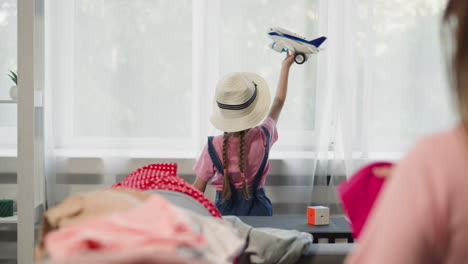 Girl-plays-with-plane-while-mother-folds-clothes-on-sofa