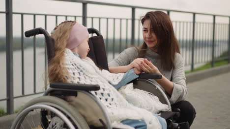 Happy-mother-holds-hand-of-little-daughter-in-wheelchair