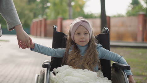 Little-girl-spins-wheel-of-wheelchair-holding-hand-of-mother