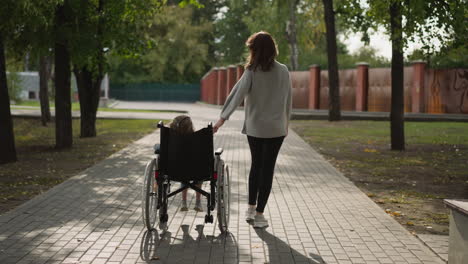 Woman-walks-on-road-moving-wheelchair-with-little-daughter