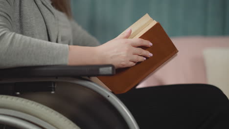 Hands-of-woman-in-wheelchair-flipping-pages-of-brown-book