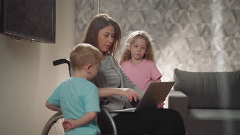 Mother-shows-kids-pictures-on-laptop-sitting-in-wheelchair