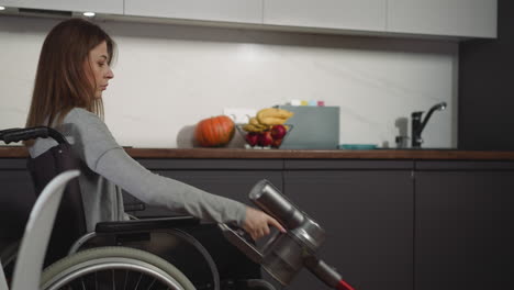 Serious-young-woman-sits-in-wheelchair-near-table-cleaning