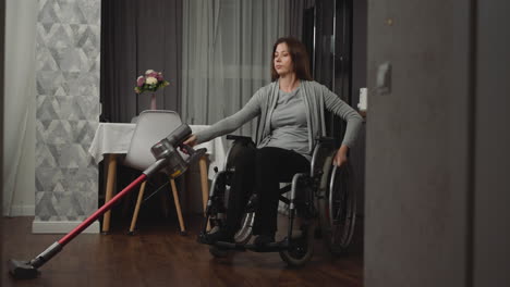 Junge-Hausfrau-Saugt-Boden-Im-Zimmer-Und-Bewegt-Sich-Im-Rollstuhl