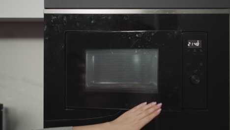 Female-hands-put-plate-with-dish-in-built-in-microwave-oven