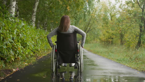 Young-woman-in-wheelchair-after-injury-walks-in-park-in-rain