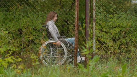 Young-woman-in-wheelchair-moves-in-park-past-old-mesh-fence