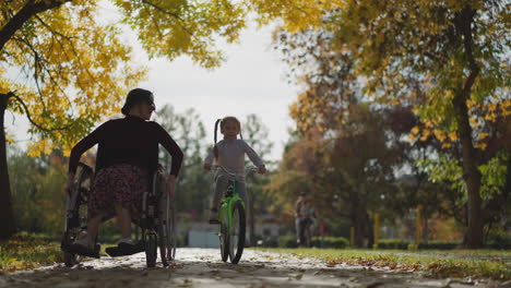 Young-aunt-in-wheelchair-and-niece-on-bicycle-rest-in-park