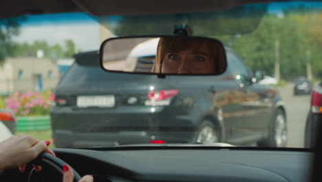 Reflection-of-woman-in-rear-view-mirror-on-windshield-in-car
