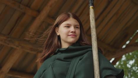 Smiling-girl-in-green-cloak-stands-in-gazebo-holding-spear