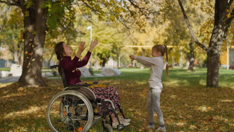 Mädchen-Wirft-Herbstblätter-über-Mutter-Im-Rollstuhl