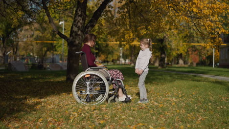 Mother-in-wheelchair-and-daughter-communicate-in-park