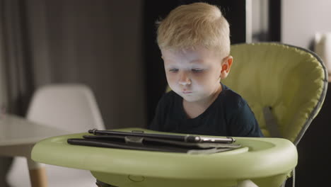 Tranquil-little-boy-watches-video-via-tablet-in-high-chair