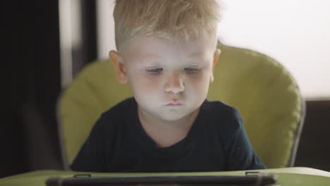 Toddler-child-looks-at-tablet-screen-sitting-in-high-chair