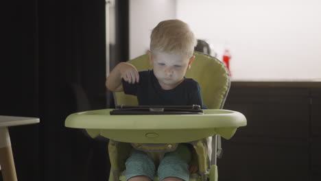 Smart-boy-touches-tablet-screen-opening-app-in-high-chair