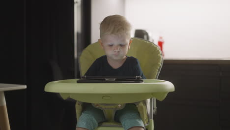 Kleiner-Junge-Wählt-Video-Auf-Tablet-Und-Schwingt-Beine-Auf-Stuhl