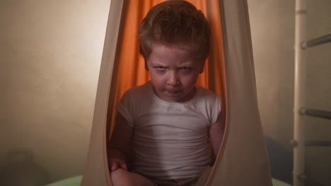 Upset-little-boy-ready-to-cry-sitting-in-orange-hammock