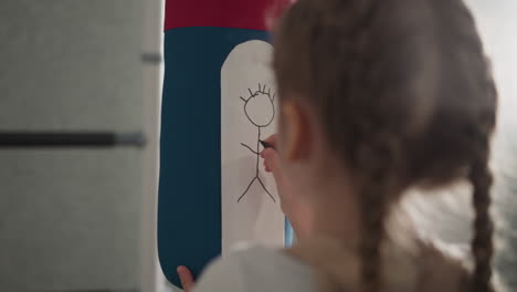 Kleines-Mädchen-Mit-Zöpfen-Zeichnet-Menschliche-Figur-Auf-Boxsack