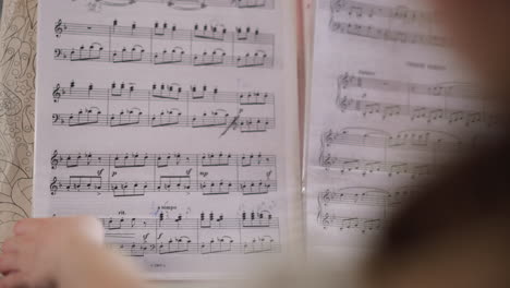 Young-musician-flips-through-sheet-music-playing-piano