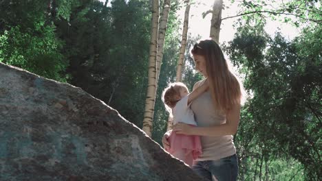 Young-beautiful-mother-and-daughter-playing-in-the-woods-near-big-stone
