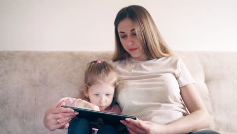 CU-4k-Young-attractive-mother-and-sweet-daughter-are-sitting-on-the-couch-and-training-using-a-tablet-computer