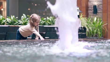 Slow-motion-Little-sweet-girl-playing-with-water-near-fountain-Sprays-water-with-a-hand