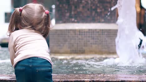 CU-Back-view-Slow-motion-Little-sweet-girl-playing-with-water-near-fountain-Sprays-water-with-a-hand