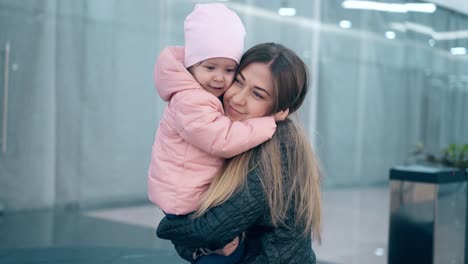 CU-4k-Young-beautiful-mother-hugs-a-little-daughter-they-are-in-a-business-center-Smiling