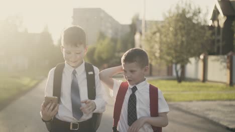 Cu-Verfolgung:-Zwei-Schulkinder-Gehen-Nach-Der-Schule-Nach-Hause,-Reden,-Halten-Ein-Smartphone-In-Ihren-Händen,-Lächeln-Und-Umarmen-Sich