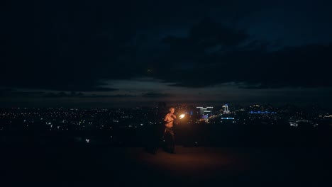 Young-blond-male-does-tricks-with-fire-breaths-fire-in-the-middle-of-the-night-with-city-skyline-in-background