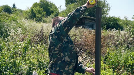 mature-man-measures-height-of-fence-metal-pole-with-tape