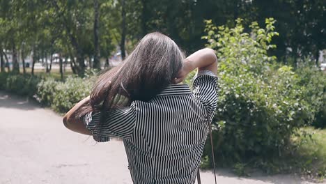 backside-view-brunette-girl-walking-in-park-fixes-long-hair