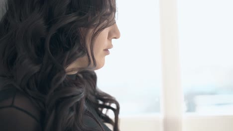 young-woman-with-dark-hair-poses-at-window-close-side-view