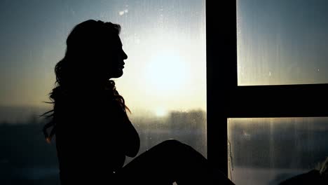 silhouette-of-long-haired-woman-near-window-at-sunset
