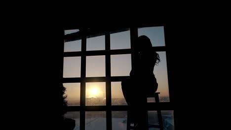 silhouette-of-sad-lady-sitting-near-large-window-in-dusk