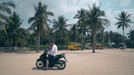 guy-sits-on-girl-stands-by-scooter-on-square-against-palms